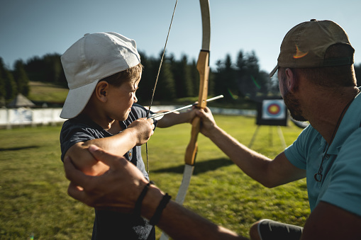 Little boy with hat learning outdoors how to use bow with instructor