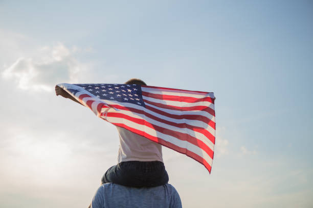 маленький мальчик позволяет американскому флагу летать в его руках на ветру на зеленом поле. 4 июля сша день независимости. конституция и де - july 4 стоковые фото и изображения