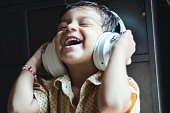 Indian Smiling little boy using phone.indoor shoot at home. The 3 year old boy is wearing white headphones.