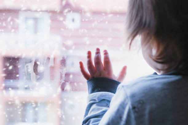 Little boy looking out of the window on a snowy day stock photo