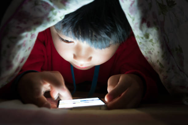 Little boy on cell phone under duvet Little boy on cell phone under duvet lpay game online stock pictures, royalty-free photos & images