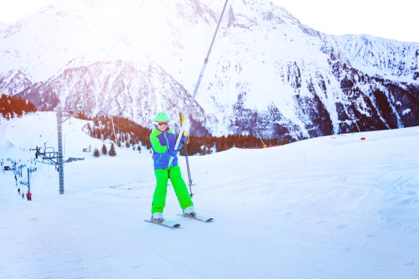 Little boy on the ski drag lift rope over sunset Happy little boy lifting on the ski drag lift rope in bright sport outfit over sunset light near mountain peak t bar ski lift stock pictures, royalty-free photos & images