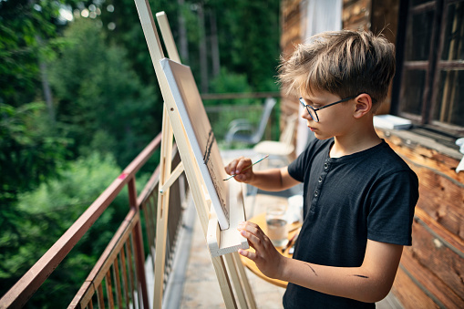 Little boy painting on easel.\nNikon D850