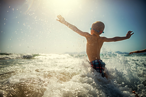 Little boy having fun splashing in sea waves. Sunny day of summer vacations. 