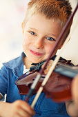 Portrait of a little boy playing violin. Very shallow depth of field. The boy aged 3 is smiling into the camera.