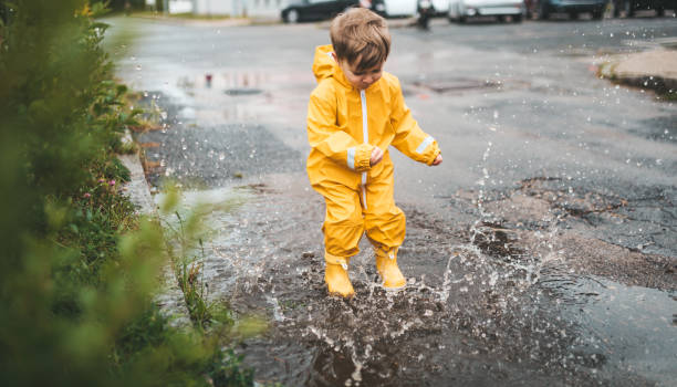 little boy plays in the rain and jumps into the water paints stock photo
