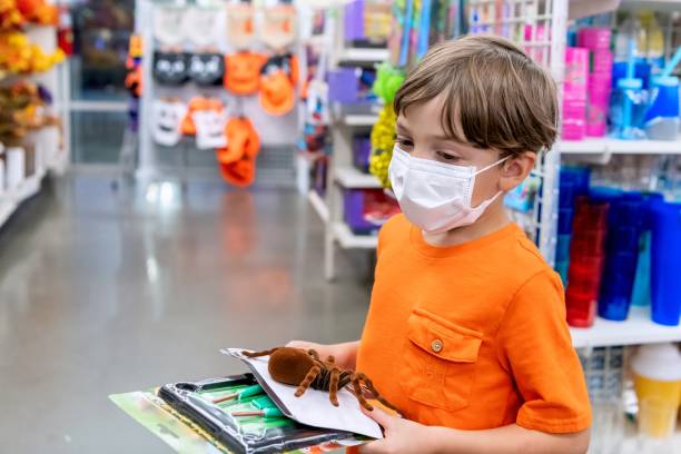 little boy shopping for halloween toys wearing a protective face mask - toy store stockfoto's en -beelden