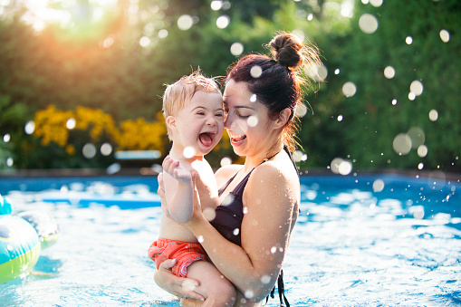 Three years old Little boy with Down syndrome having fun in the swimming pool with his family.  Her mother holds him in her arms. Color and horizontal Photo was taken in Quebec Canada.