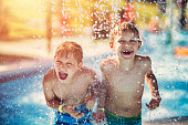 Little boys having fun in splash pool in a waterpark. Laughing and screaming boys are being splashed by water.
