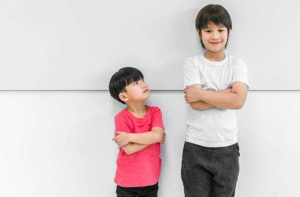 Little child boy standing arms crossed and looking face of tall child at standing arms crossed and smiling stock photo