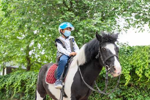 Little Child Boy With Protective Face Mask Riding Pony Horse