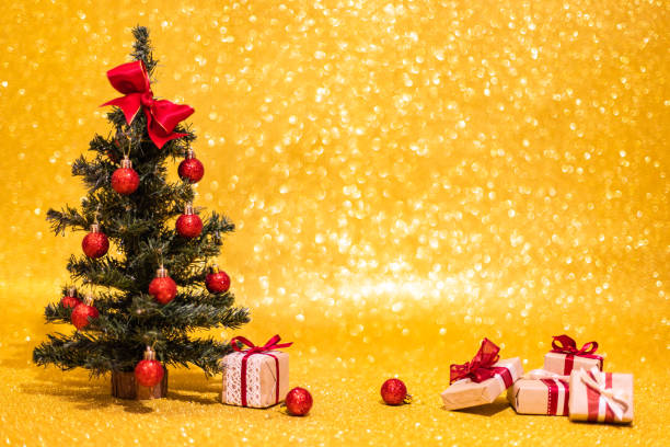 Little Christmas tree with some decoration ball and xmas gifts in small boxes on golden shining bokeh background, image with copy space stock photo