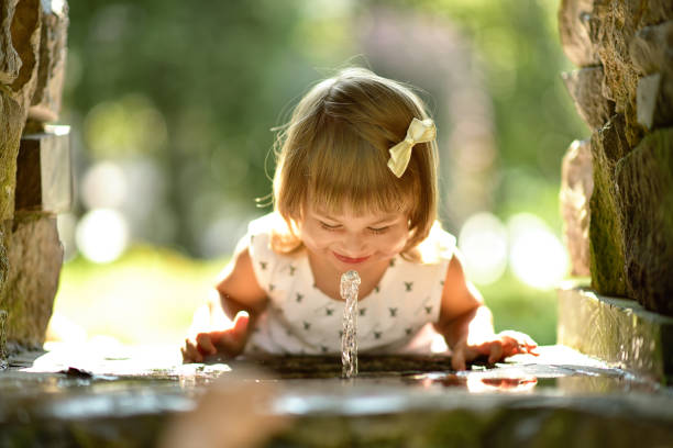 Little cute baby girl drinks eater from fountain stock photo