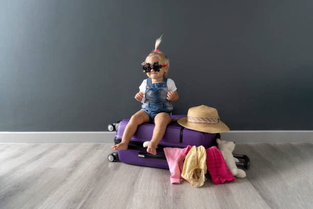 little cute barefoot blond baby girls in black sunglasses sits on a violet suitcase and waits for summer holiday travel trip in abroad, copy space. - foster home bag imagens e fotografias de stock