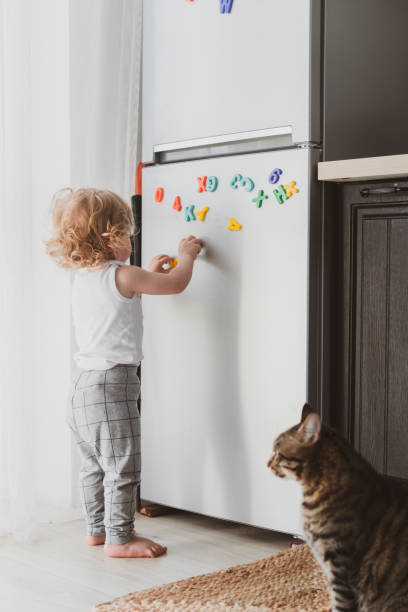 little cute toddler playing with toy letters on the fridge stock photo