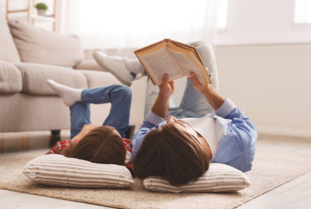 niña y padre disfrutando del libro juntos, tumbado en el suelo - leer fotografías e imágenes de stock
