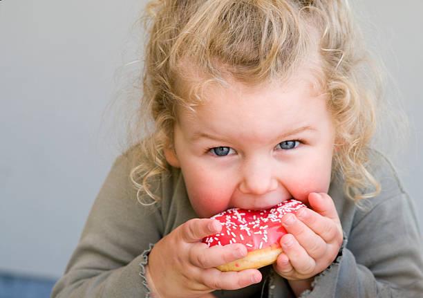 Little girl eating jelly-glazed donut with sprinkles stock photo