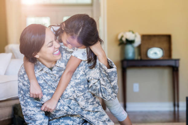 Little girl gives army mom a big hug Excited little girl hugs her mom from behind. The girl is happy to have her military mom home from military assignment. veterans returning home stock pictures, royalty-free photos & images