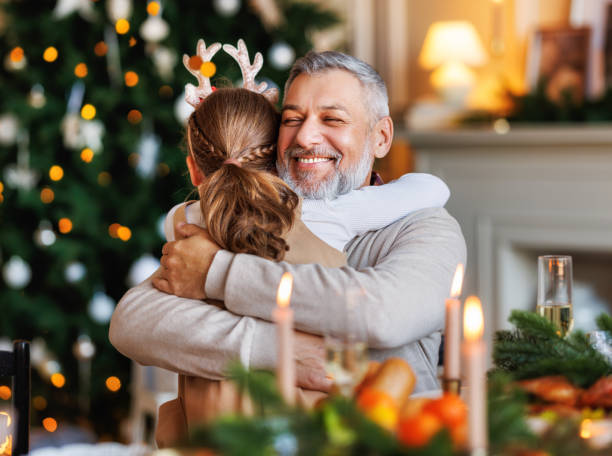 Little girl granddaughter embracing happy smiling grandfather during Christmas dinner at home stock photo