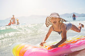 Little girl jumping on inflateable raft being splashed by waves in sea.
