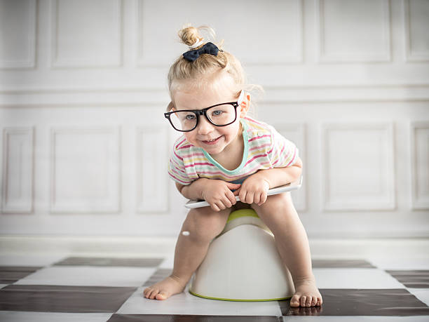 A little girl holding a tablet while sitting on white potty stock photo