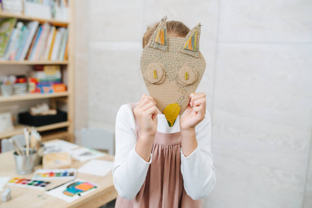 Little girl holdng cardboard handmade fox mask over her face stock photo