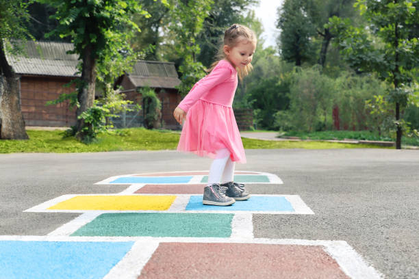 Little girl in a pink dress playing hopscotch on playground outdoors, children outdoor activities Little girl in a pink dress playing hopscotch on playground outdoors, children outdoor activities asian girls feet stock pictures, royalty-free photos & images