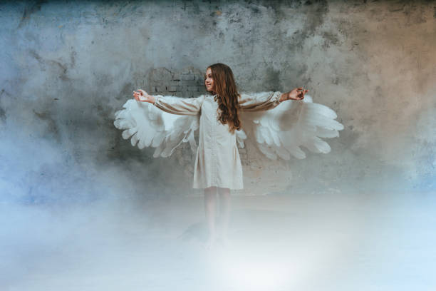 Little girl in ethnic dress wearing angel wings standing in white smoke Little girl in ethnic dress wearing angel wings standing in white smoke raising her hands and looking up. angel 8 stock pictures, royalty-free photos & images