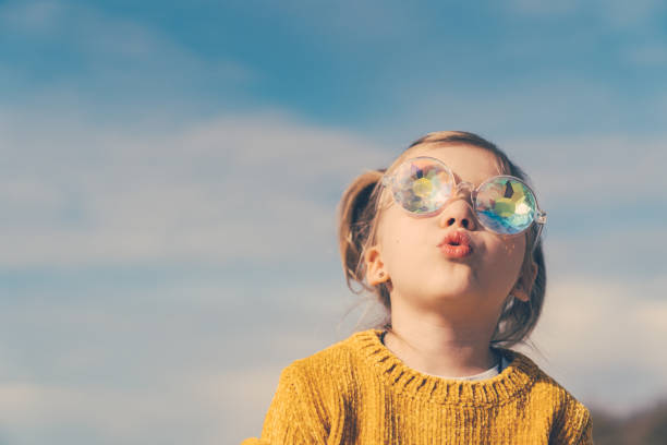 little girl in funny kaleidoscope glasses is looking to the sky with open mouth and curiosity. stock photo