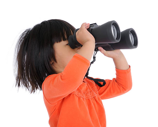 Little girl in orange shirt looking through black binoculars stock photo
