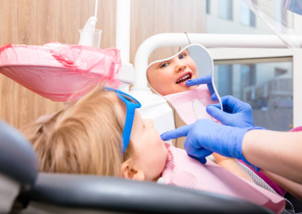 Little girl looking at cured teeth thru the mirror in pediatric dental clinic Dentist showing to little girl cured tooth in pediatric dental clinic. Child is sitting in a dental chair inspecting her teeth looking thru tooth-shaped mirror rotten teeth in children stock pictures, royalty-free photos & images