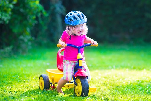 Children riding a bike. Kids enjoying a bicycle ride. Little preschooler girl having fun outdoors. Active toddlers play in the garden. Summer fun in a park. Child wearing safety helmet.