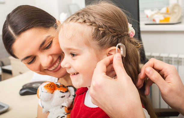 маленькая девочка пациентка очень рада, что теперь она будет слышать звуки окружающего мира с помощью слухового аппарата. слуховая клиника - hearing aid стоковые фото и изображения