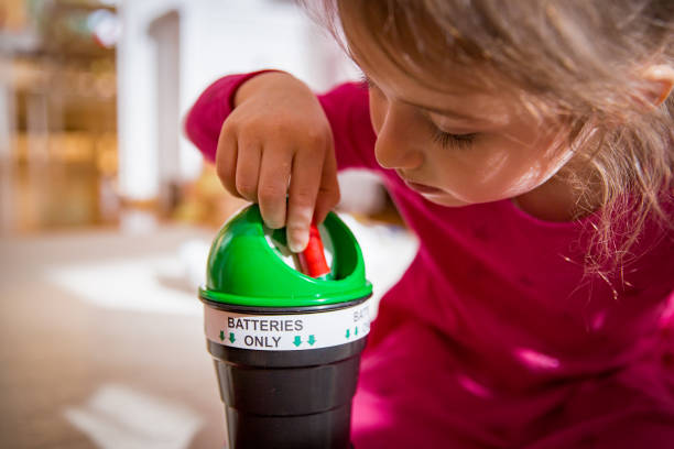Little girl putting used batteries into recycling box stock photo