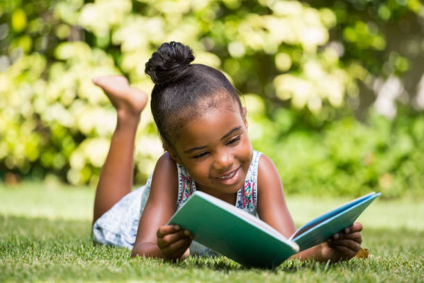 little girl reading a book at park - child reading imagens e fotografias de stock