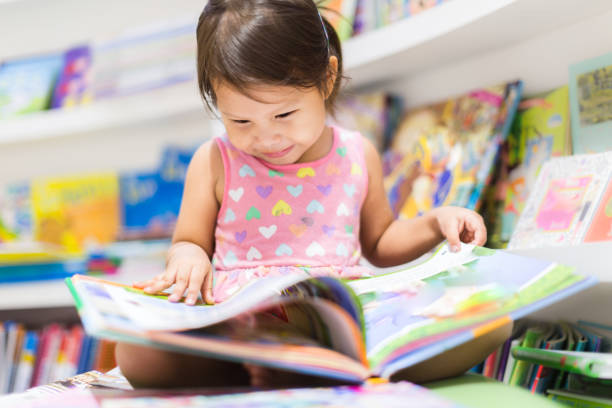 Little girl reading a book. Education. A happy child looking at a book in the library. preschool age stock pictures, royalty-free photos & images