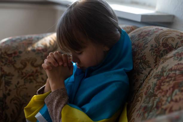little girl refugee prays with Ukrainian flag. stock photo