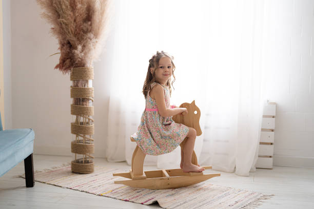 Little girl riding a toy wooden horse at home stock photo