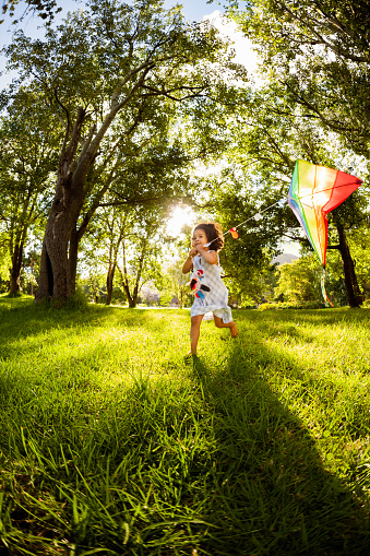 Active little girl running while holding a kite at garden. Vertical Shot. Slight motion blur due to running.