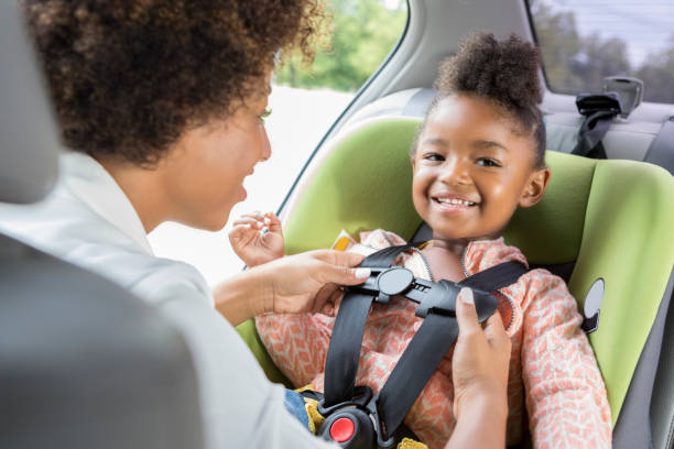 Little girl smiles as she is buckled into car seat An adorable preschool age girl looks away and smiles as her unrecognizable mother buckles her into her car seat. car safety seat stock pictures, royalty-free photos & images