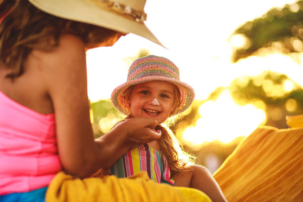 Little girl smiling at camera while her mother is applying sunscreen on her face stock photo