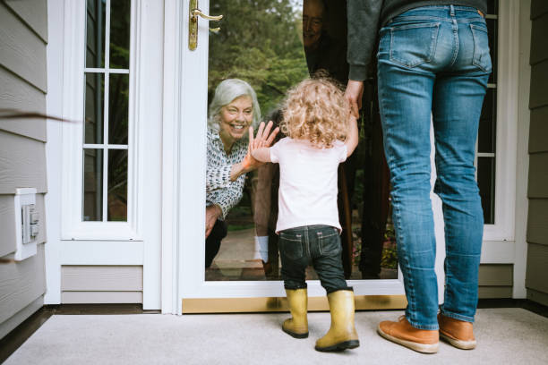 Little Girl Visits Grandparents Through Window A mother stands with her daughter, visiting senior parents but observing social distancing with a glass door between them.  The granddaughter puts her hand up to the glass, the grandfather and grandmother doing the same.  A small connection in a time of separation during the Covid-19 pandemic. quarantine stock pictures, royalty-free photos & images