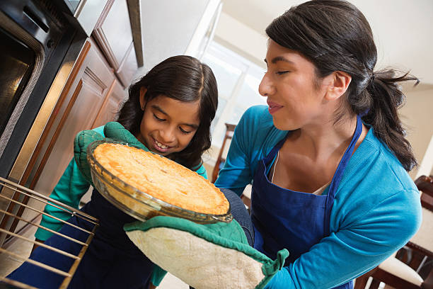 Little girl watching mother take apple pie from oven Little girl watching mother take apple pie from oven hot latino girl stock pictures, royalty-free photos & images