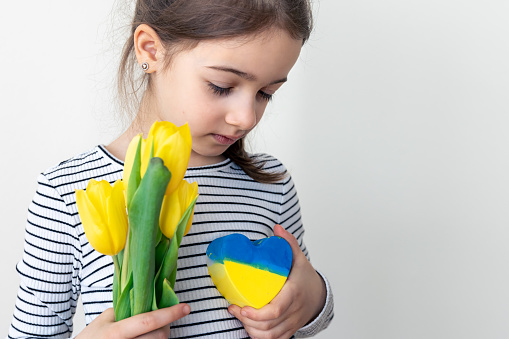 Little girl with a bouquet of yellow tulips and a heart painted in the colors of the flag of Ukraine, the concept of patriotism and love for Ukraine.