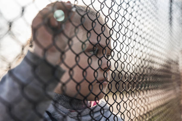 Little girl with a sad look behind a metal fence, social problems, raising children in orphanages stock photo