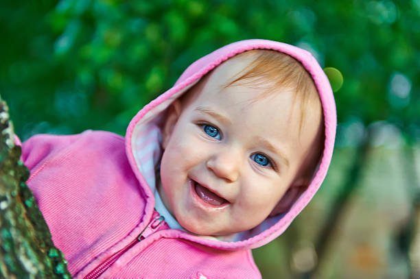 Little girl with blue eyes peered out from behind tree stock photo