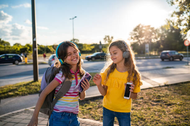 Little girls with headphones are walking and using their phones stock photo