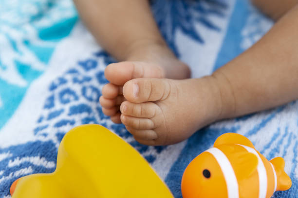 Little infant legs of a baby girl sitting on a beach towel and playing with rubber toys at summer time stock photo
