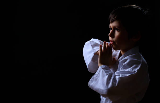 Little karate kid in white kimono isolated on dark background. Portrait of boy ready for martial arts fight. stock photo