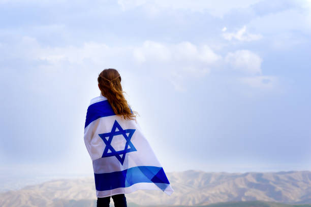 маленькая патриотическая еврейская девушка, стоящая и наслаждающаяся отличным видом на небо, долину и горы с флагом израиля, обернутой вок� - holocaust remembrance day стоковые фото и изображения
